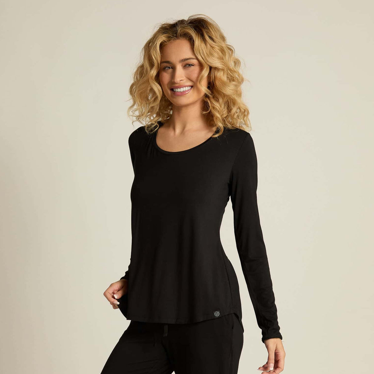 A woman wearing a black long sleeve top and matching pants, standing against a plain background