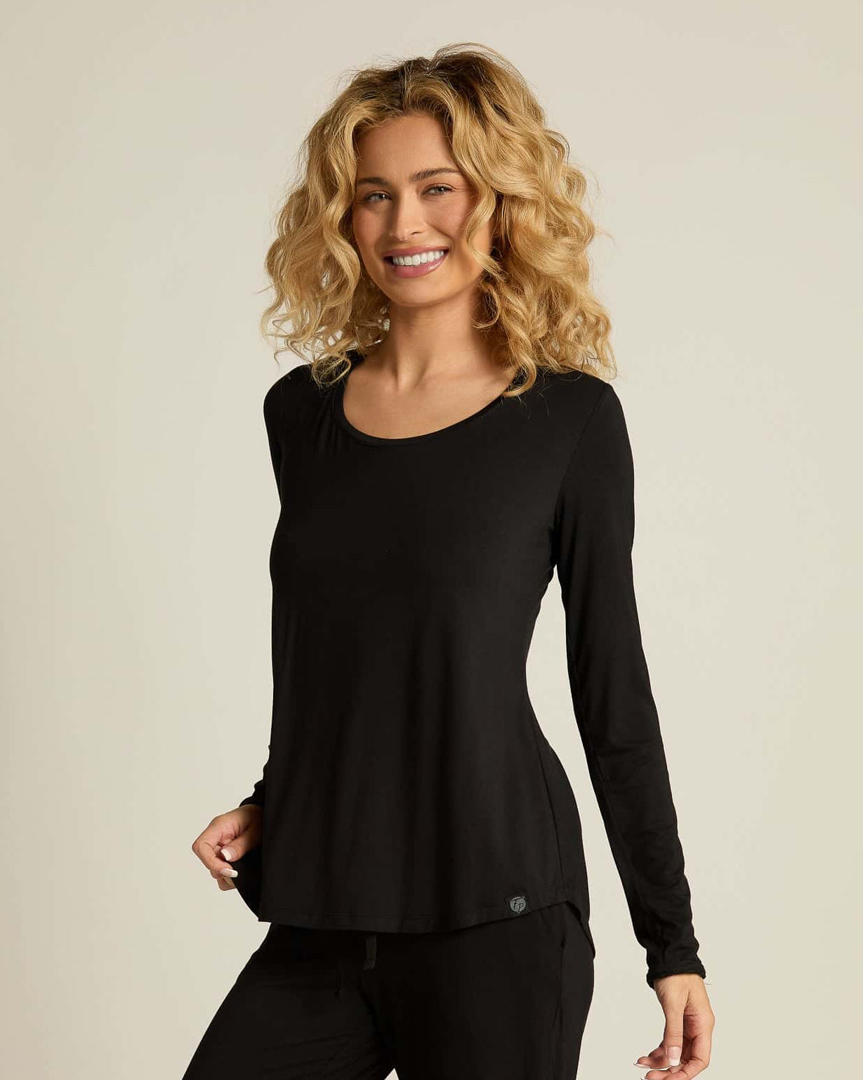 A woman wearing a black long sleeve top and matching pants, standing against a plain background