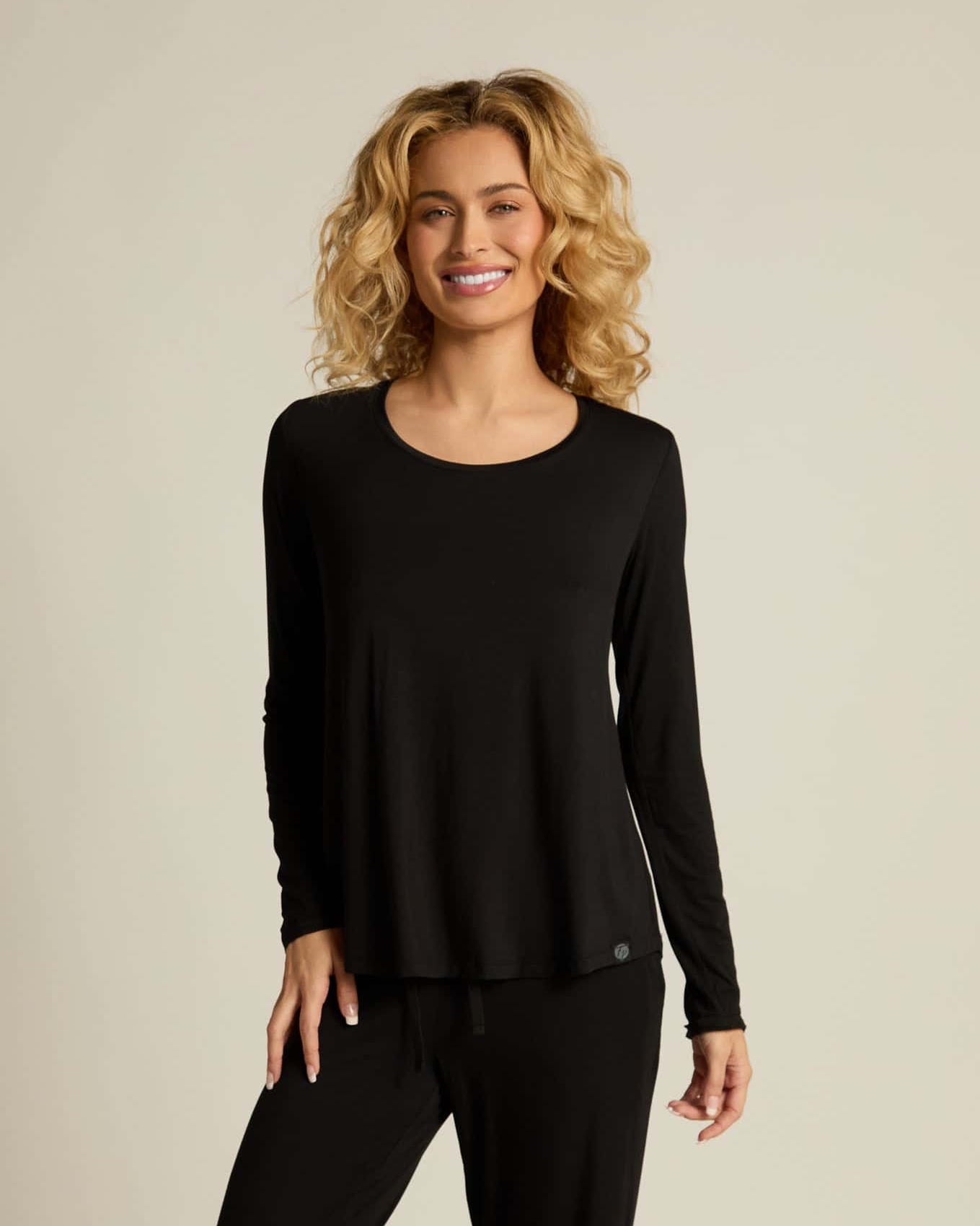 A woman wearing a black long sleeve top and matching pants, standing against a plain background