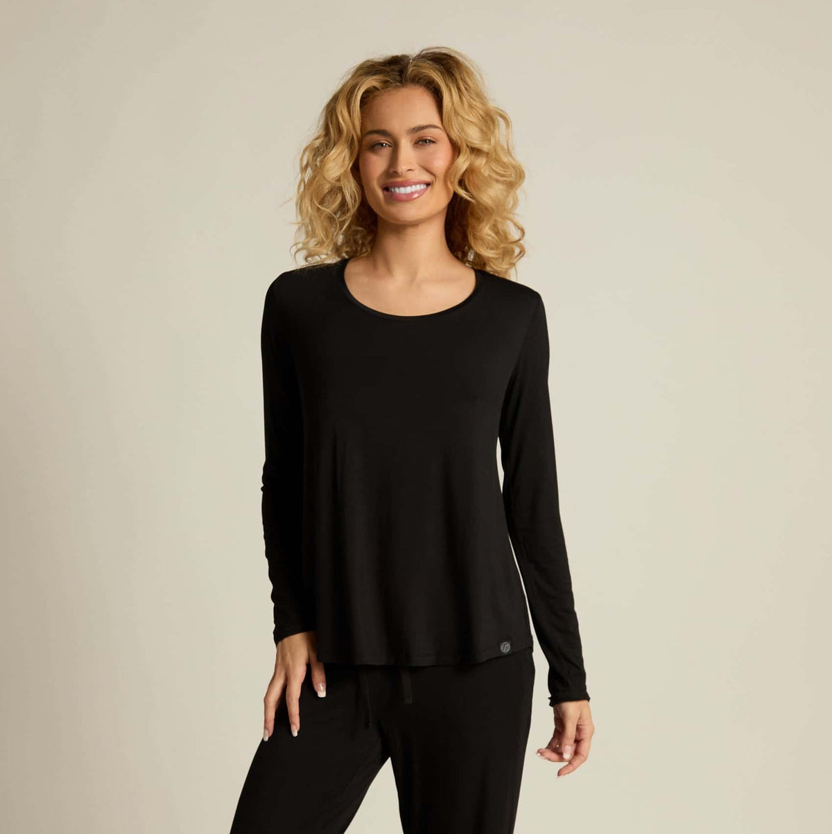 A woman wearing a black long sleeve top and matching pants, standing against a plain background