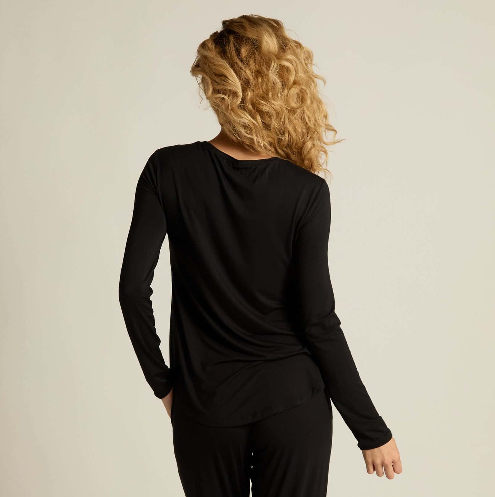 A woman wearing a black long sleeve top and matching pants, standing against a plain background