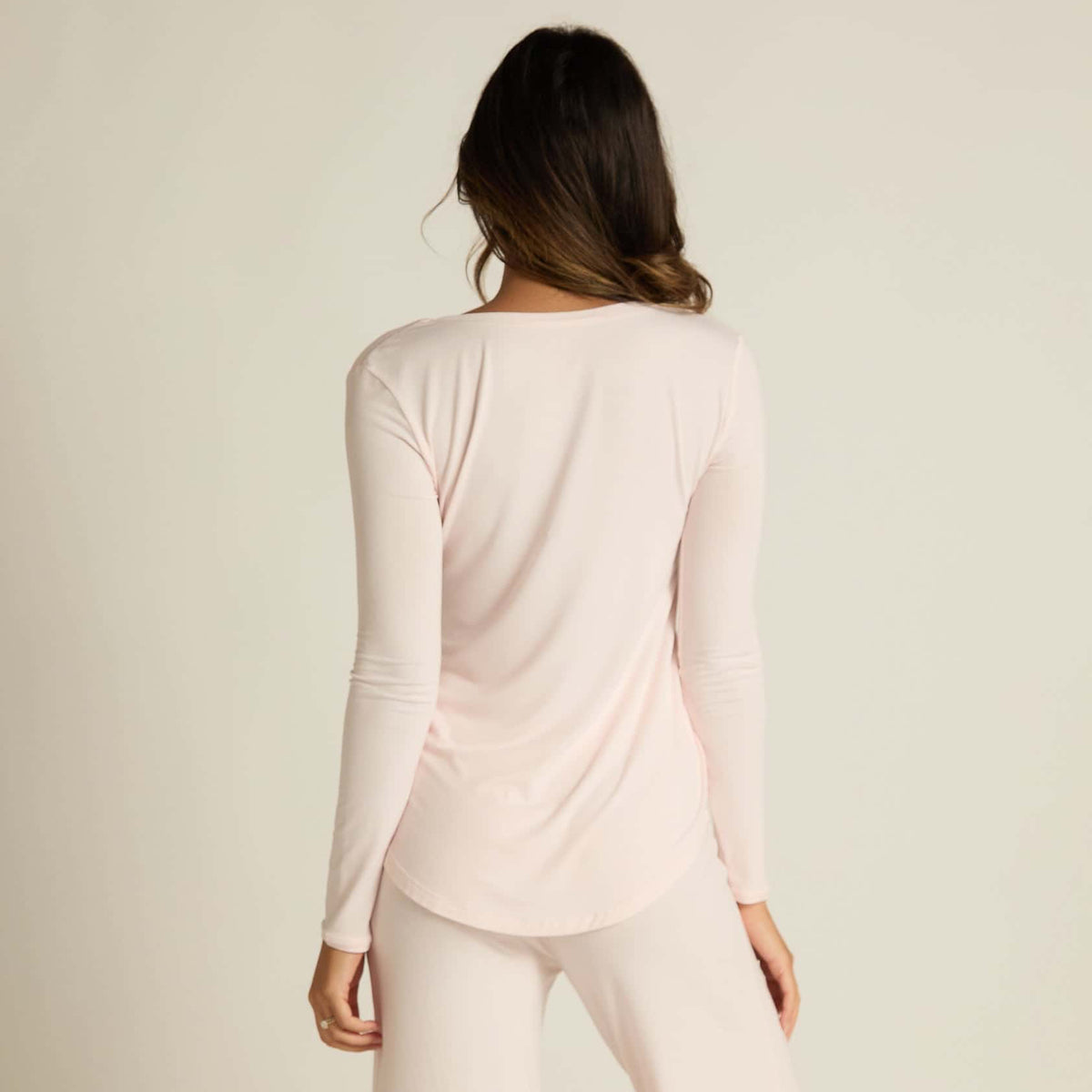 A woman wearing pink long sleeve top and matching pants, standing against a plain background