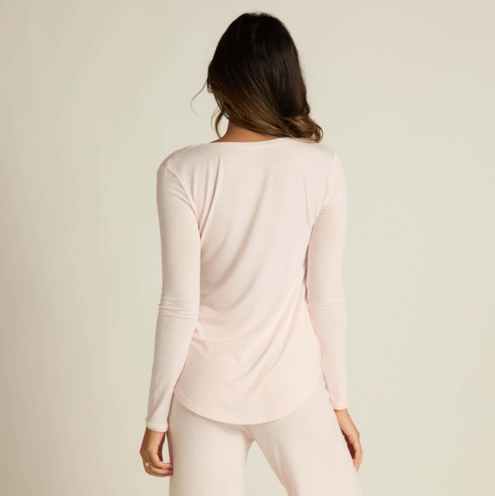 A woman wearing pink long sleeve top and matching pants, standing against a plain background