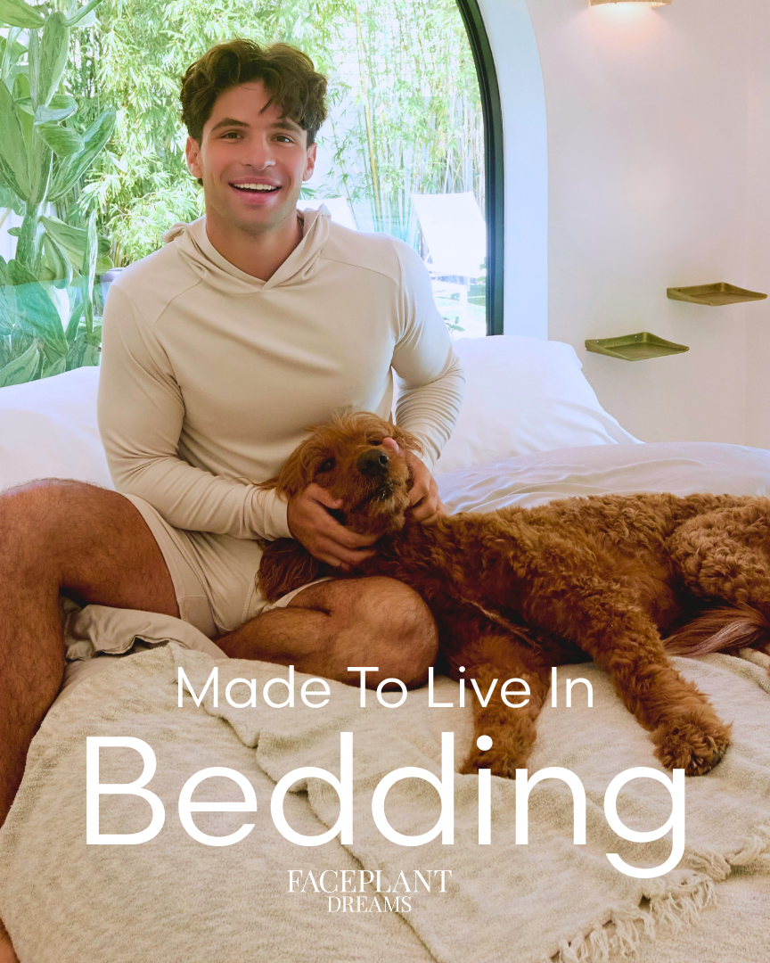 Man sitting on a bed with a dog, surrounded by bedding, in a bright room with large windows. the text 'made to live in bedding - Faceplant Dreams' is at the bottom