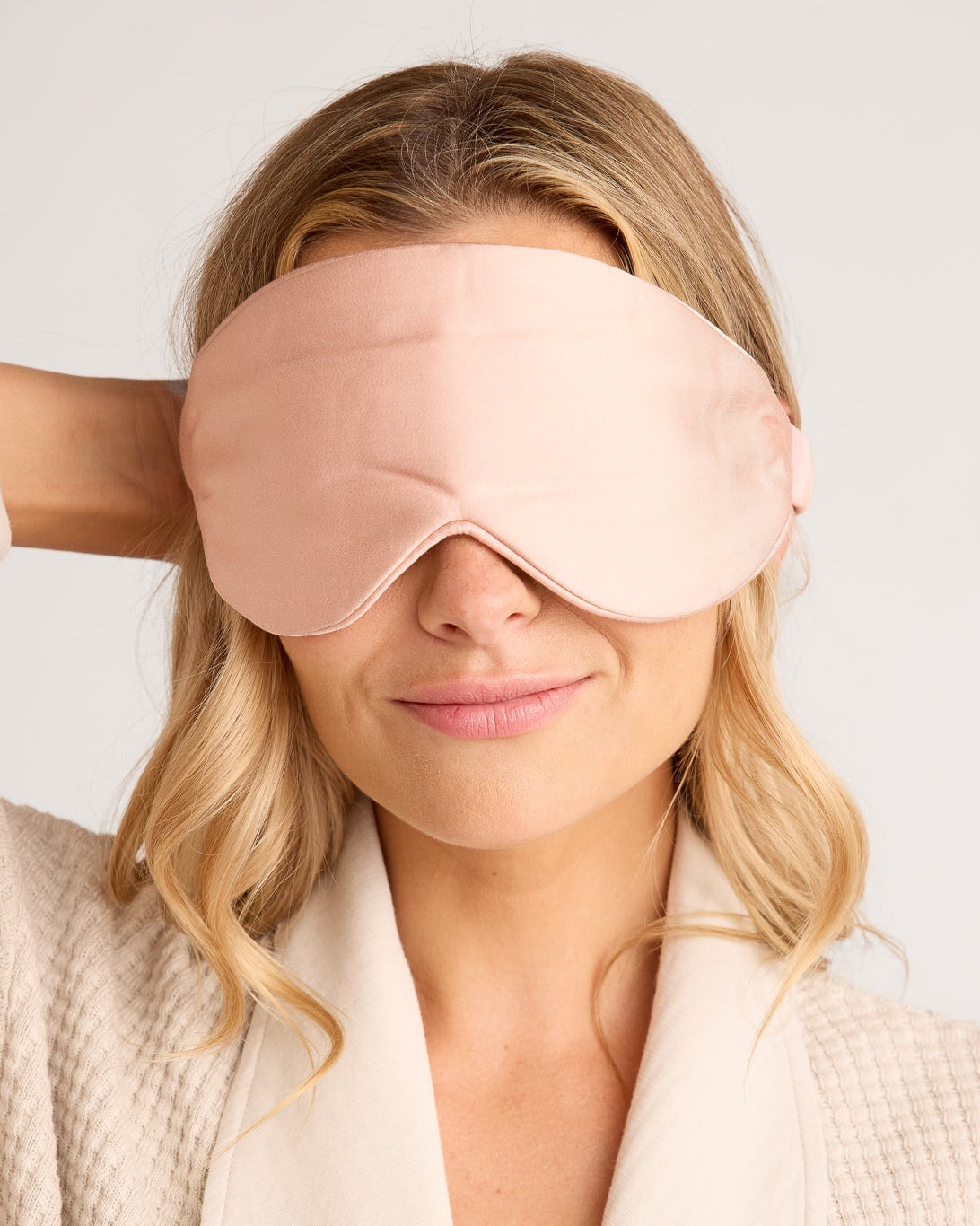 Woman wearing a pink sleep mask with a plain background