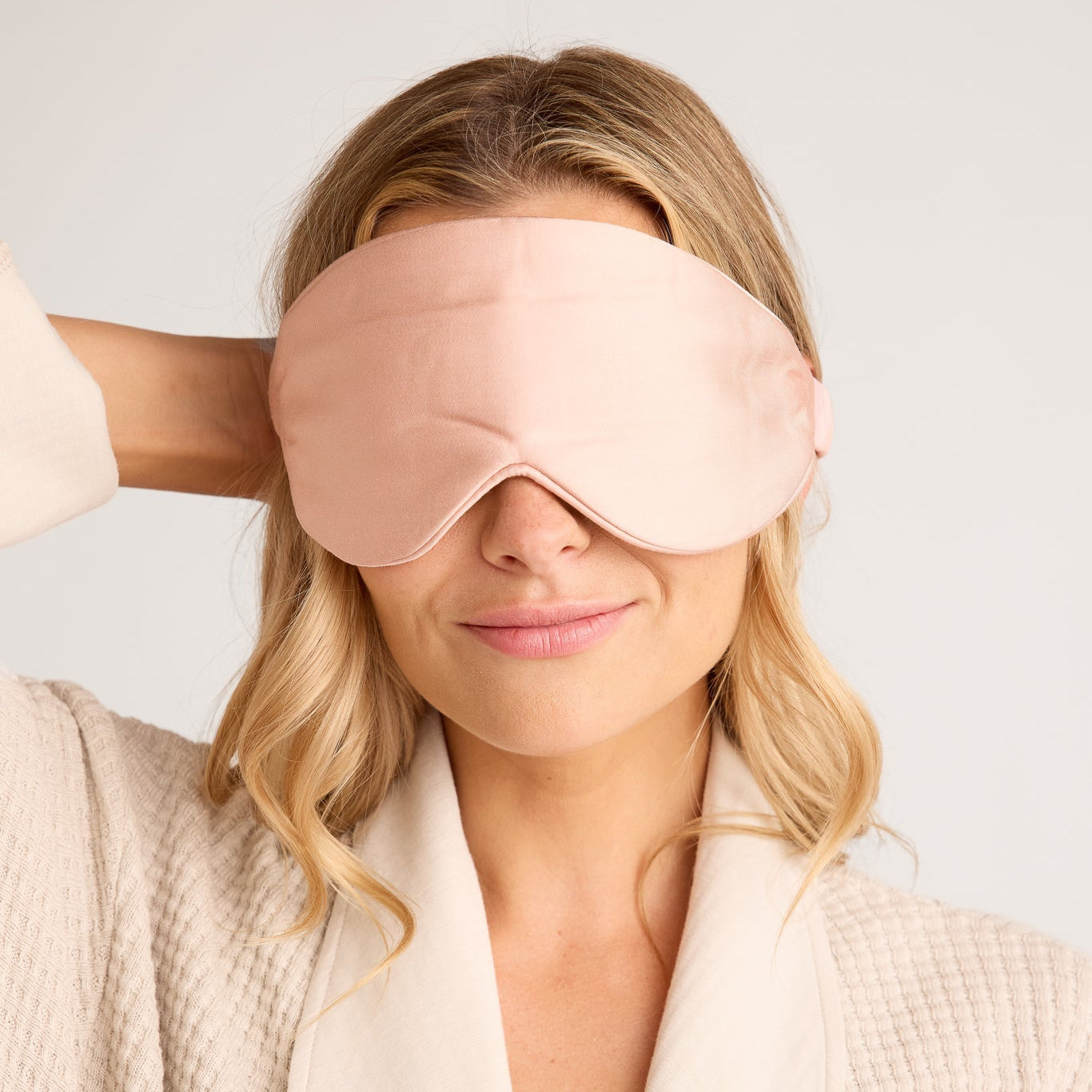 Woman wearing a pink sleep mask with a plain background
