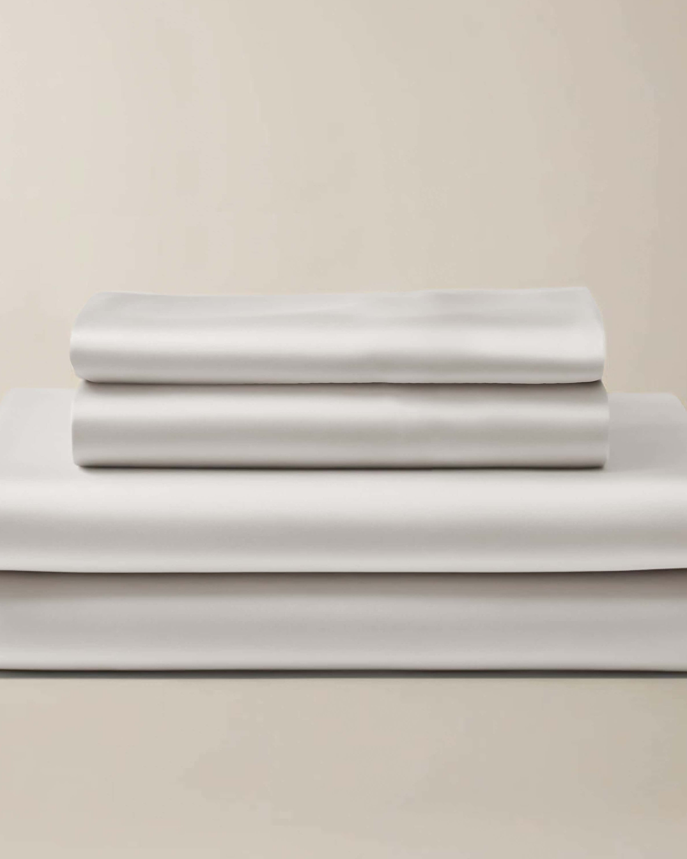 Stack of white bamboo sheet sets, including a flat sheet, a fitted sheet, and a pillowcase, presented in a neat arrangement.