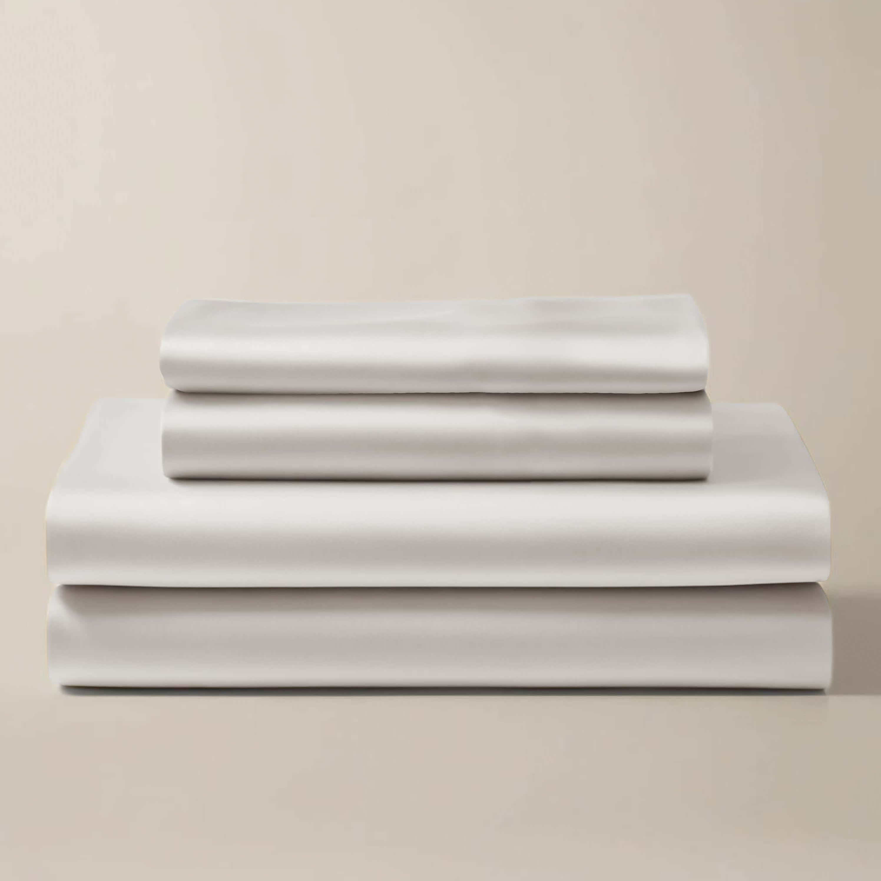 Stack of white bamboo sheet sets, including a flat sheet, a fitted sheet, and a pillowcase, presented in a neat arrangement.