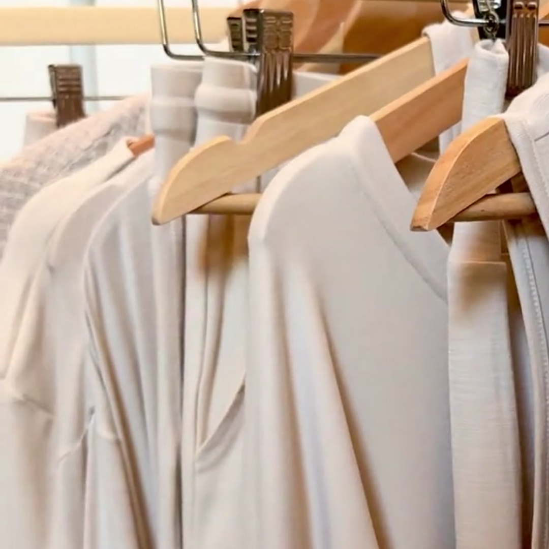 A close-up view of Faceplant's oatmeal collection of tops, bottoms, and robes hanging on wooden hangers from a clothing rack.