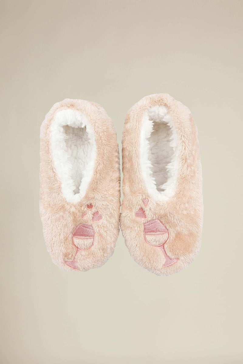 A pair of pink plush slippers designed to look like wine glasses with hearts, with the phrase 'Wine a little. Laugh a lot.