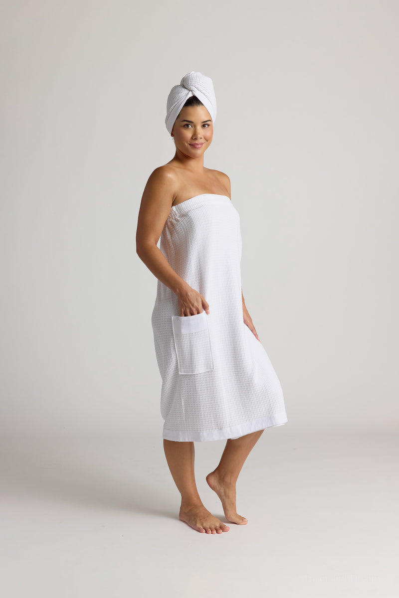 Woman wearing a white spa towel and hair wrap on a plain background