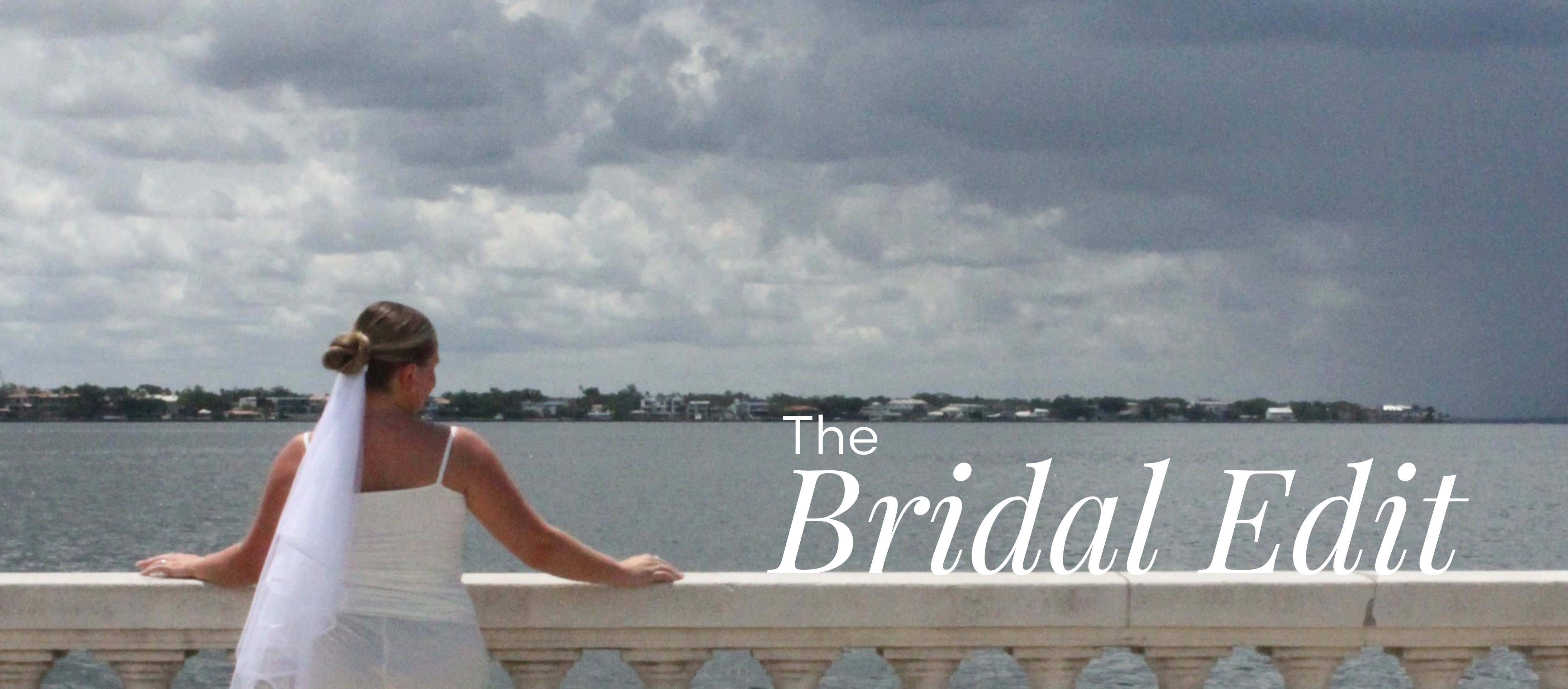 Woman in a white outfit and veil standing on a railing overlooking water with 'The Bridal Edit' text overlay.