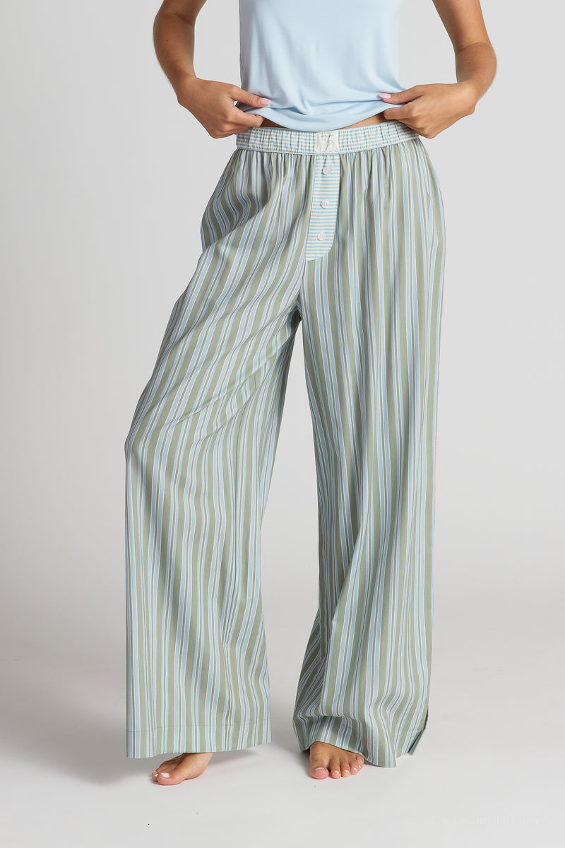 Person wearing light blue pajama top and striped green and white pajama pants on a plain background