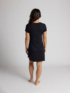 Person wearing a black dress standing against a plain background