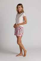 Woman wearing a light pink top and floral pajama shorts on a plain background