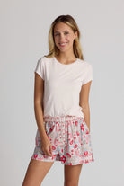 Woman wearing a light pink shirt and floral pajama shorts on a plain background
