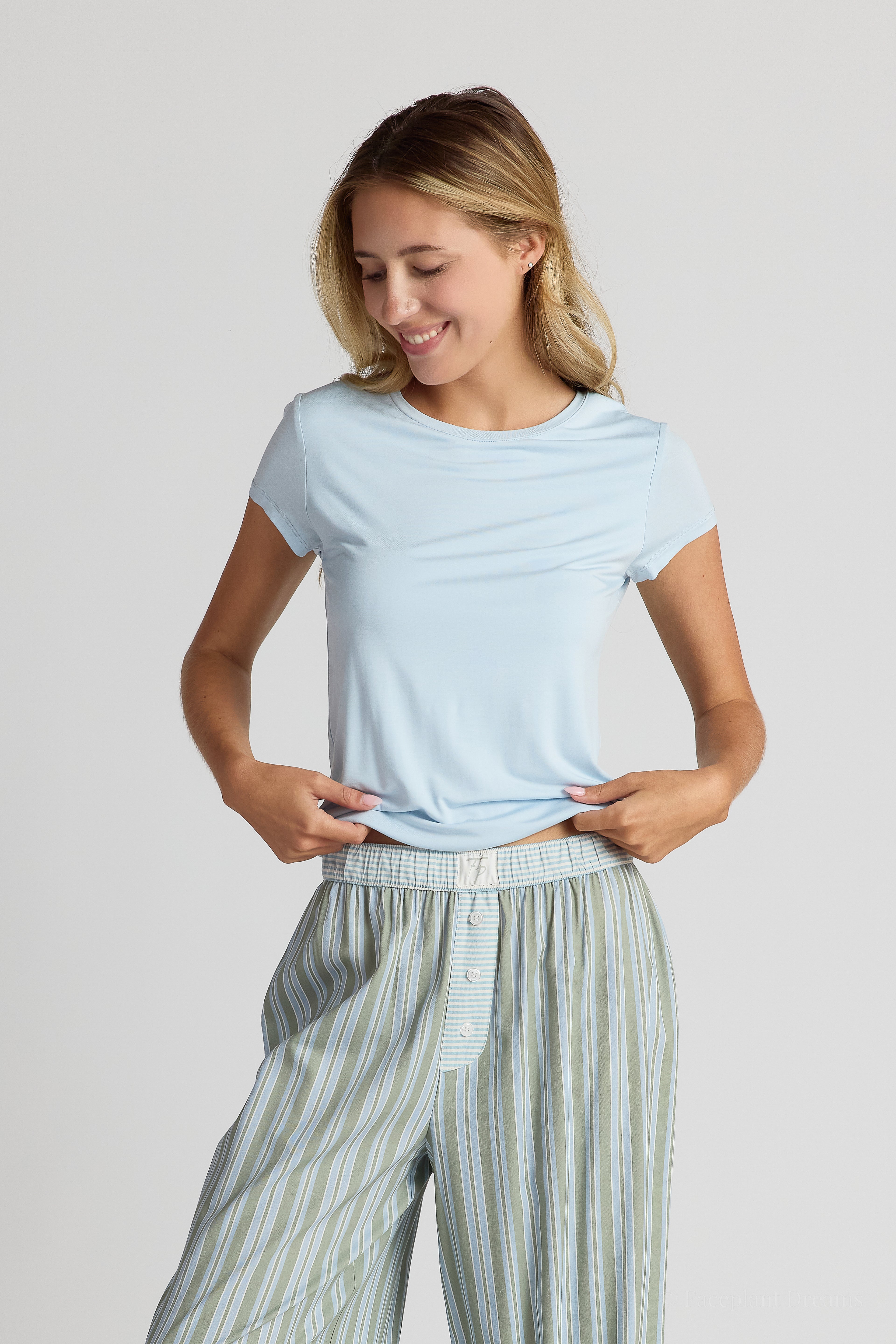 Woman wearing a light blue shirt and striped pants on a plain background