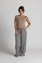 Woman wearing a brown shirt and patterned pajama pants on a plain background