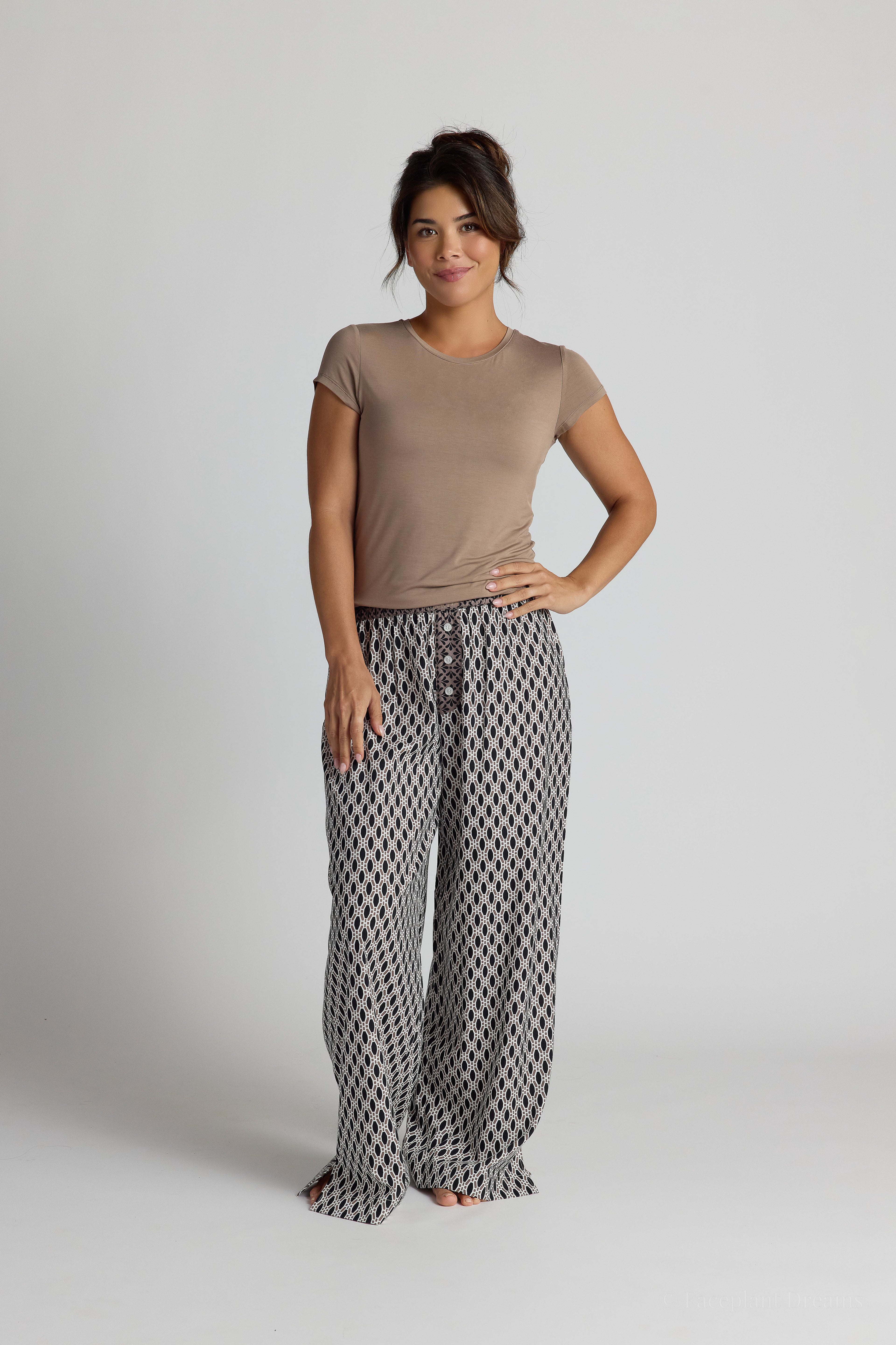 Woman wearing a brown shirt and patterned pajama pants on a plain background