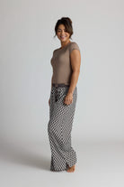 Woman wearing a brown top and patterned pajama pants on a plain background