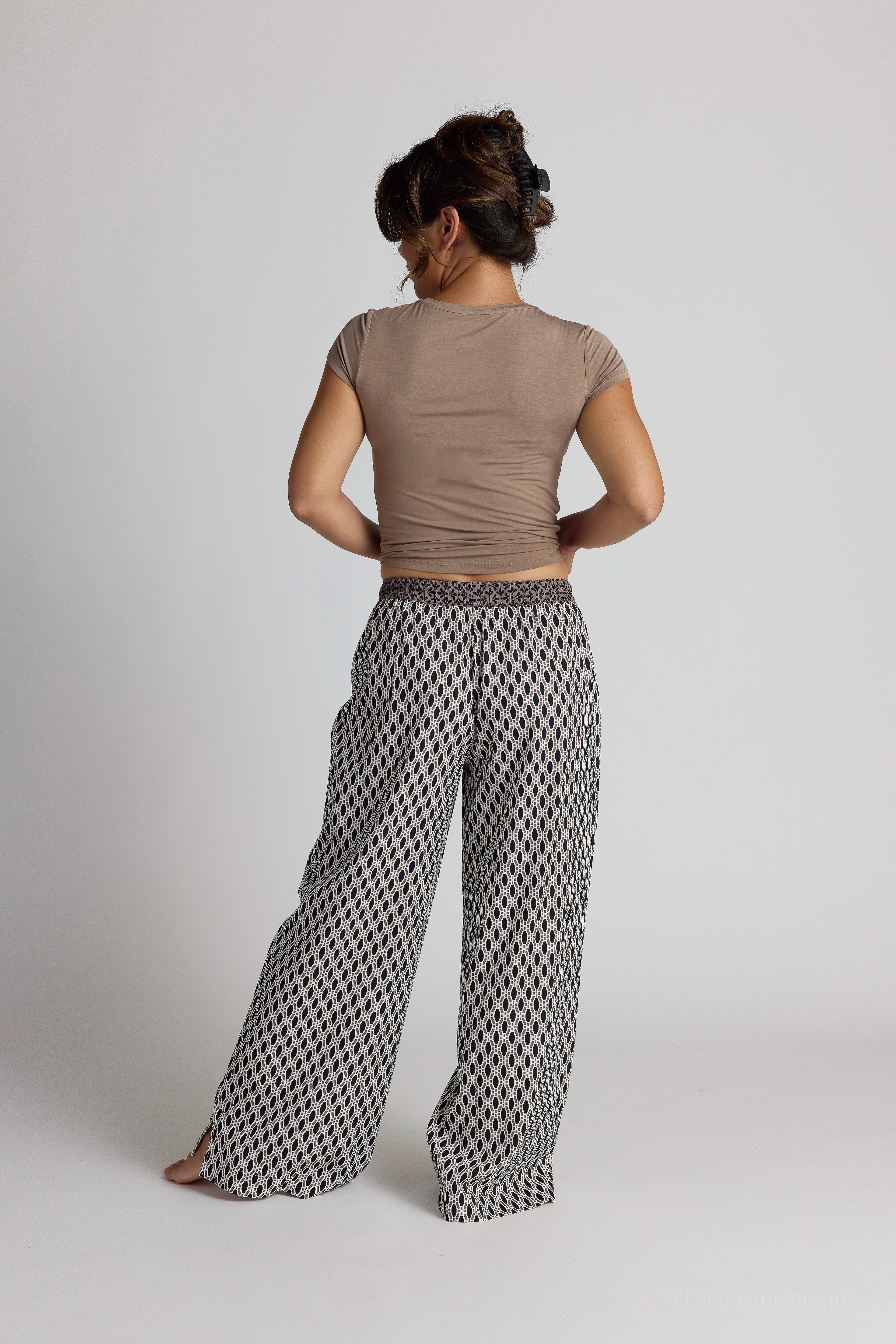 Woman wearing a brown top and patterned pajama pants on a plain background
