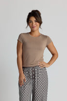 Woman wearing a brown top and patterned pajama pants on a plain background