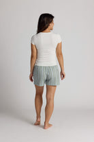 Woman wearing a white shirt and striped pajama shorts on a plain background
