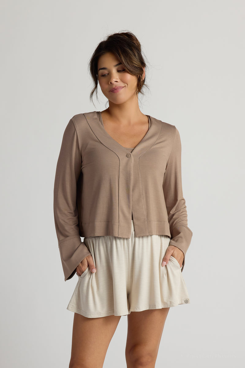 Woman wearing a brown top over a tank top and beige shorts on a plain background
