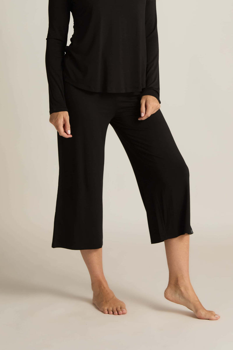 A person wearing wide-leg capri pants in a black color paired with a matching long-sleeve top.