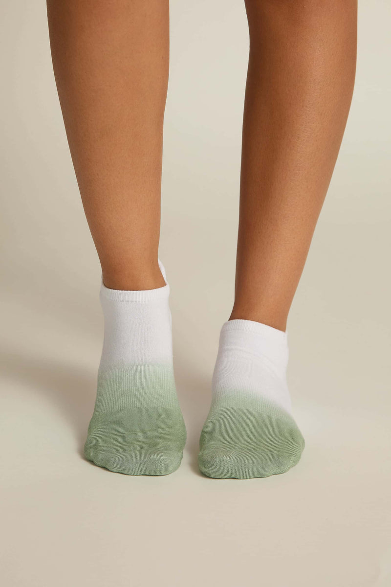 A pair of white ankle socks with a green ombre design on the toes and heel, worn on human feet.