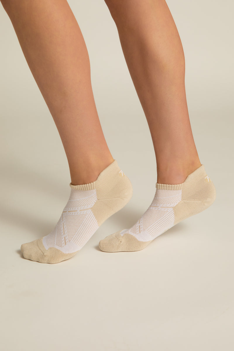 A pair of beige ankle socks with padding at the toe and heel areas, displayed on a person's feet against a white background.