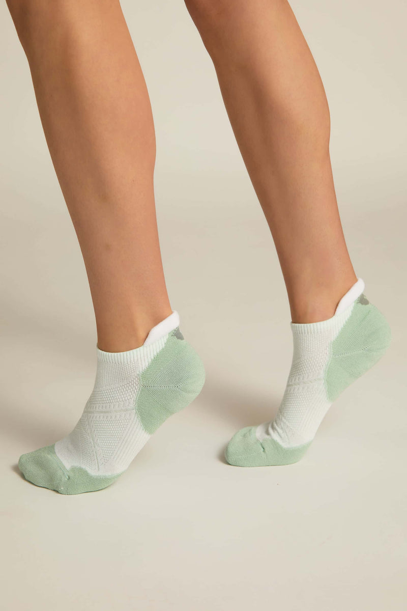 A pair of white and aqua ankle socks with padding at the toe and heel areas, displayed on a person's feet against a white background.