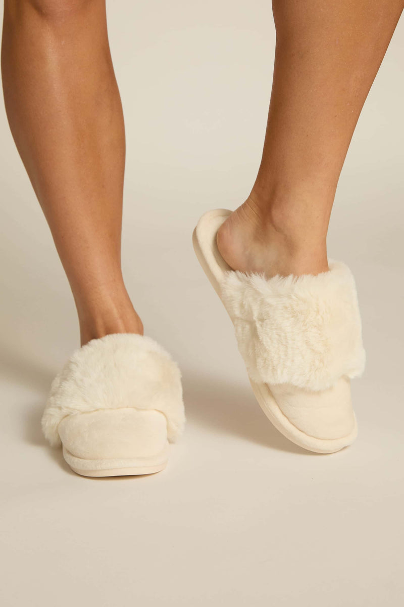 A pair of ivory furry slippers worn on human feet, showing the plush upper and the sole 