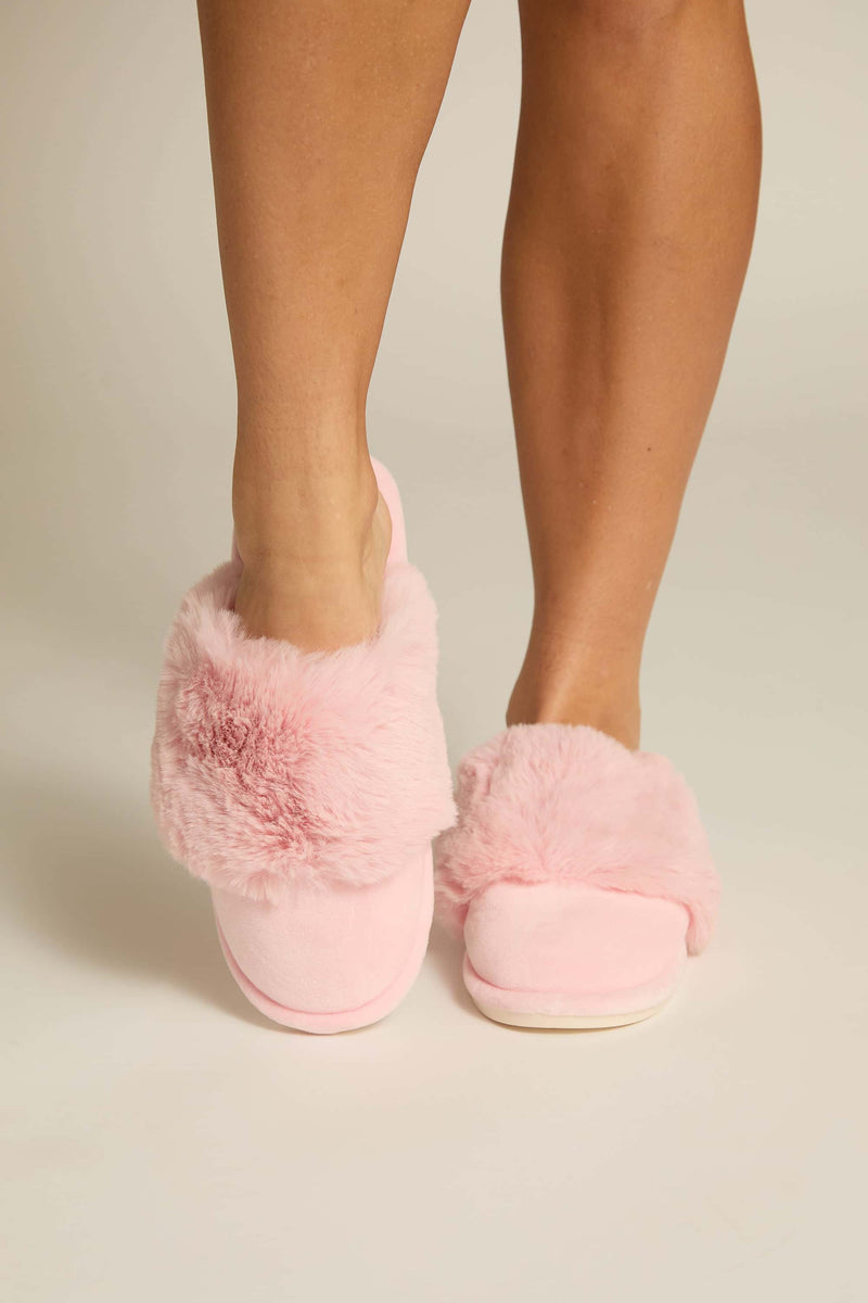 A pair of pink furry slippers worn on human feet, showing the plush upper and the sole 