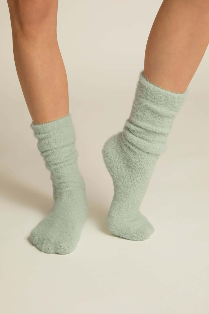 A pair of aqua fuzzy lounge socks worn on human legs, standing against a white background.