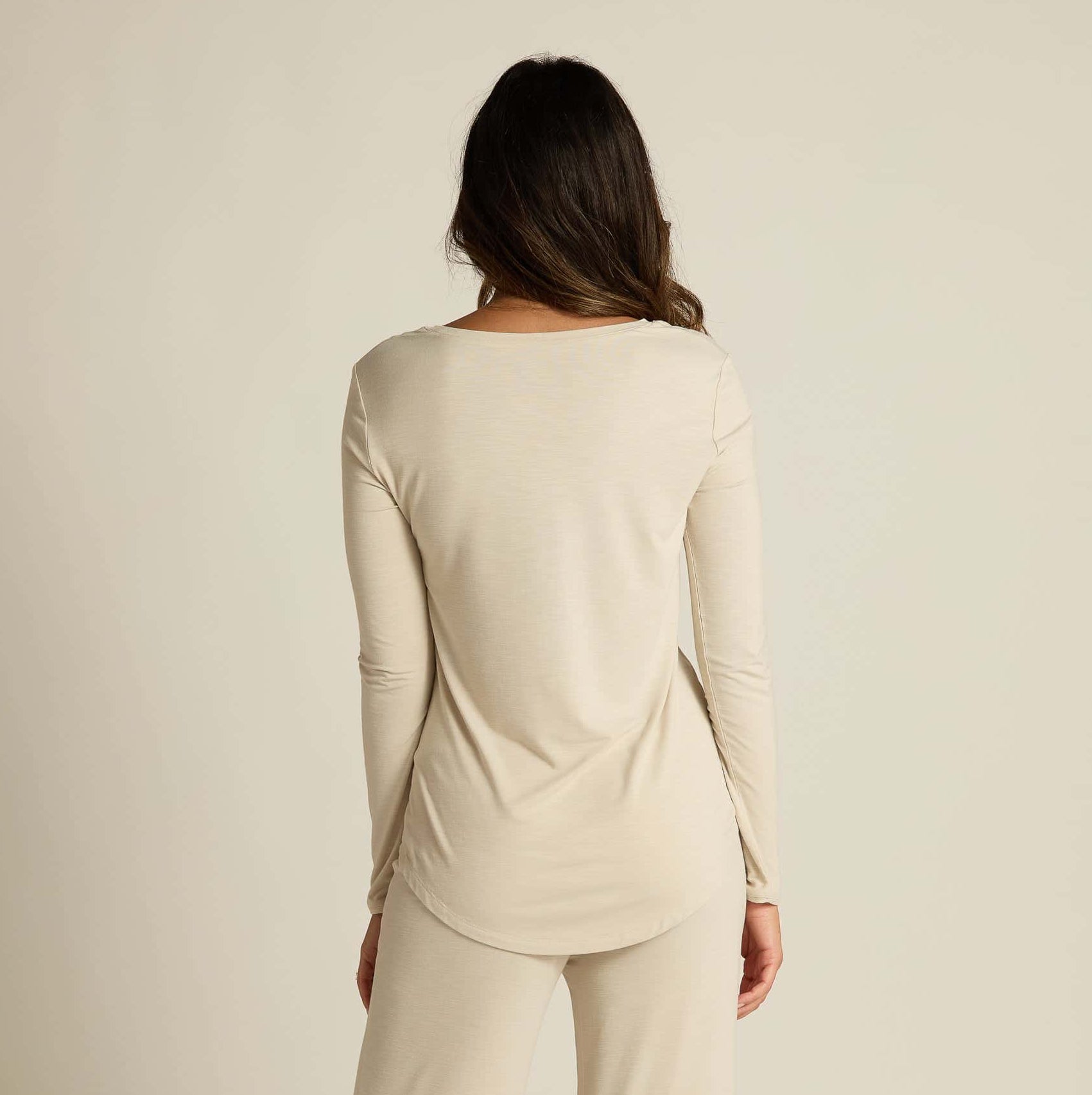 A woman wearing a beige long sleeve top and matching pants, standing against a plain background