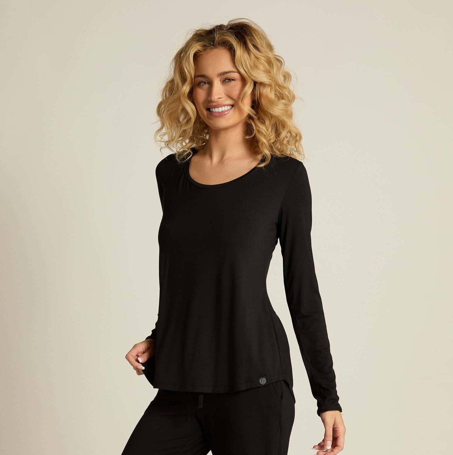 A woman wearing a black long sleeve top and matching pants, standing against a plain background