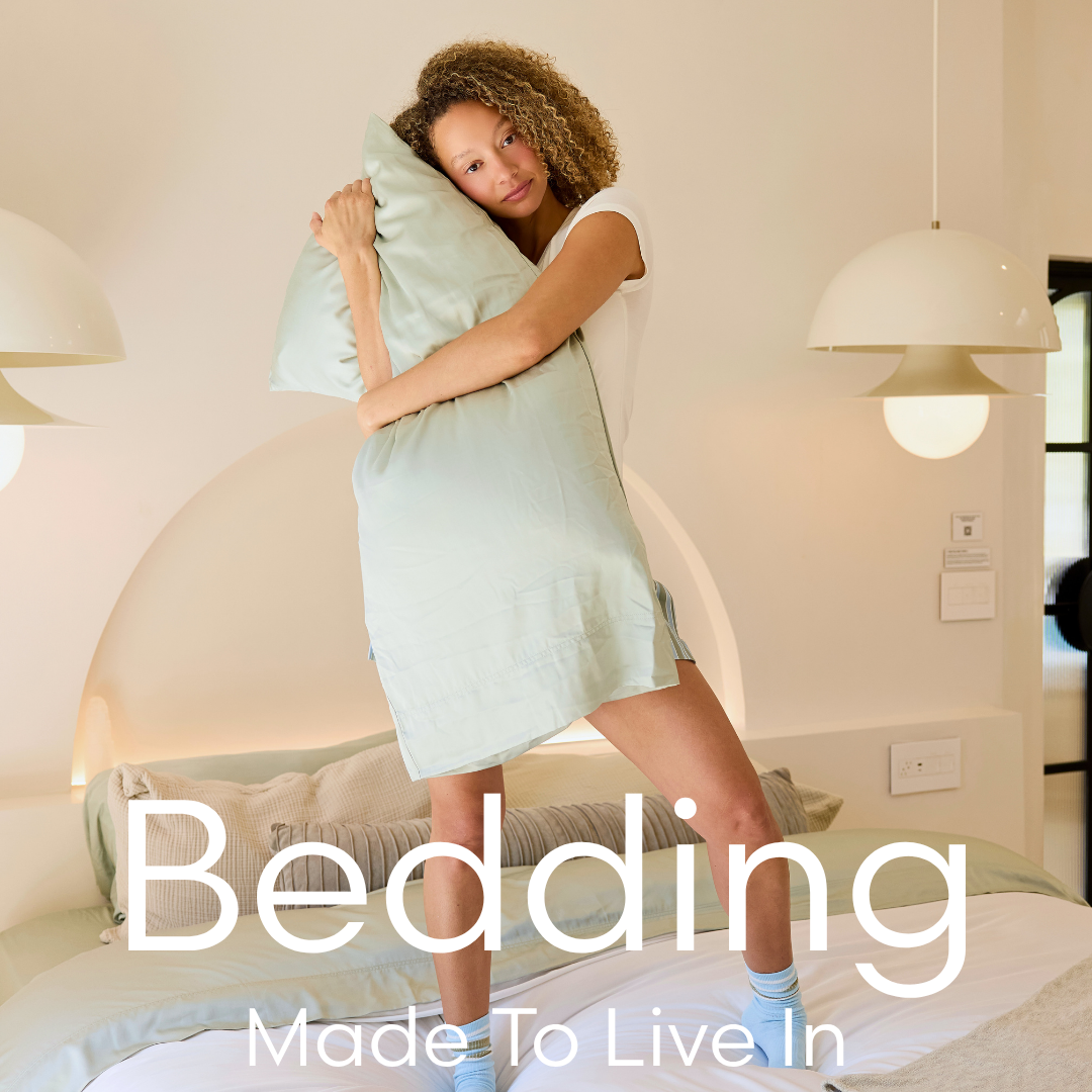 Woman hugging a pillow with 'Bedding Made To Live In' text overlay in a bedroom setting.