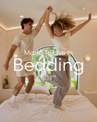 Two people jumping on a bed with 'Made To Live In Bedding' text overlay.