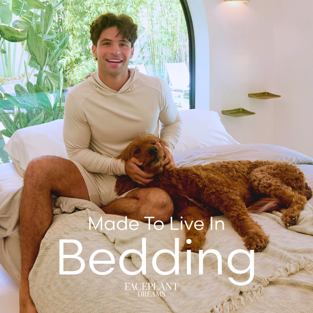 Man sitting on a bed with a dog, surrounded by bedding, in a bright room with large windows. the text 'made to live in bedding - Faceplant Dreams' is at the bottom