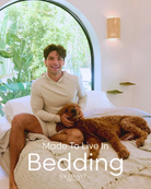 Man sitting on a bed with a dog, surrounded by bedding, in a bright room with large windows. the text 'made to live in bedding - Faceplant Dreams' is at the bottom