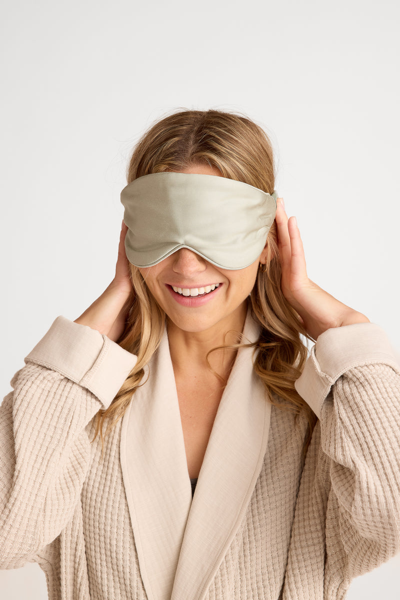 Woman wearing a sage green sleep mask against a white background
