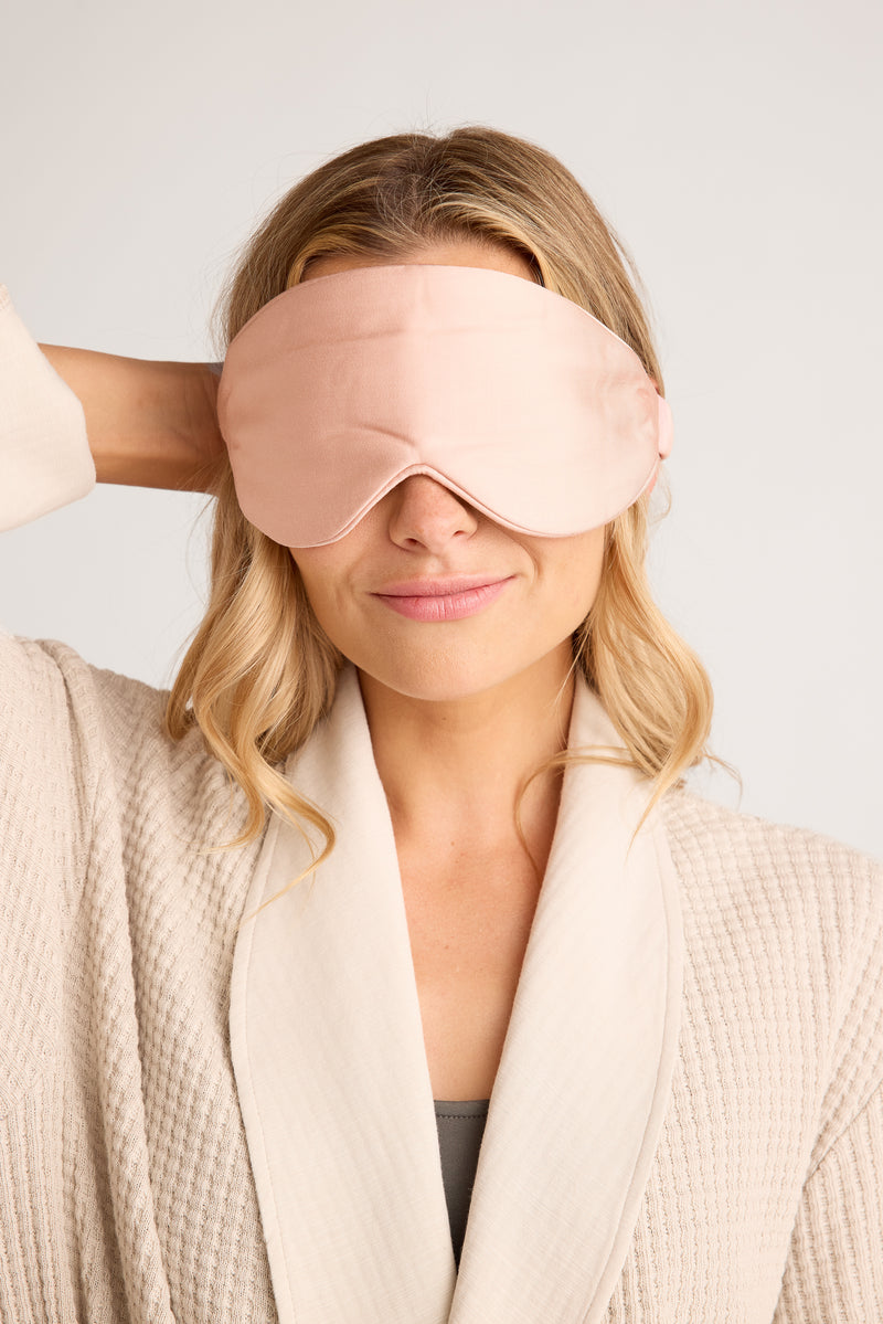 Woman wearing a pink sleep mask with a plain background