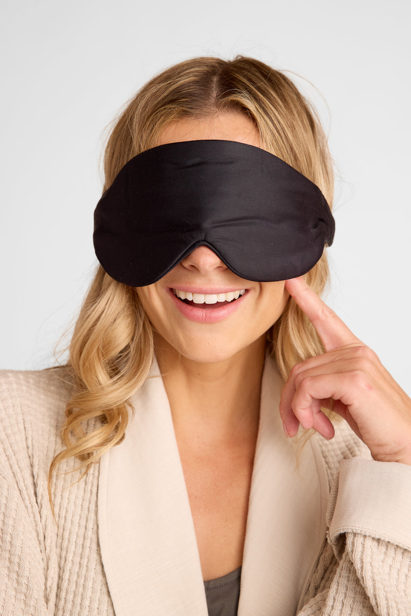 Woman wearing a black sleep mask with a neutral background