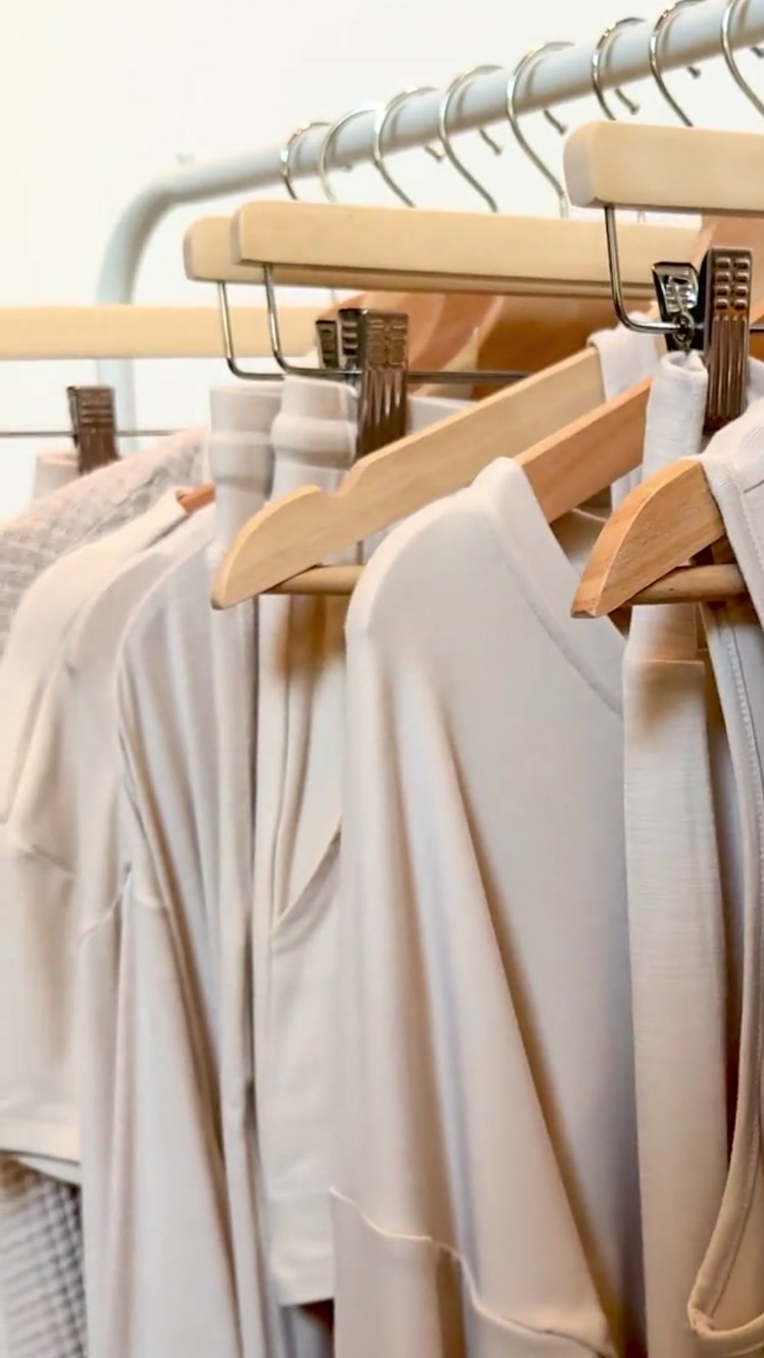 A close-up view of Faceplant's oatmeal collection of tops, bottoms, and robes hanging on wooden hangers from a clothing rack.